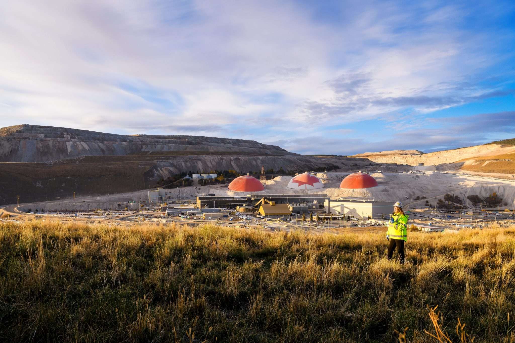 Worker in high visibility gear stands in front of a mining operation in B.C.